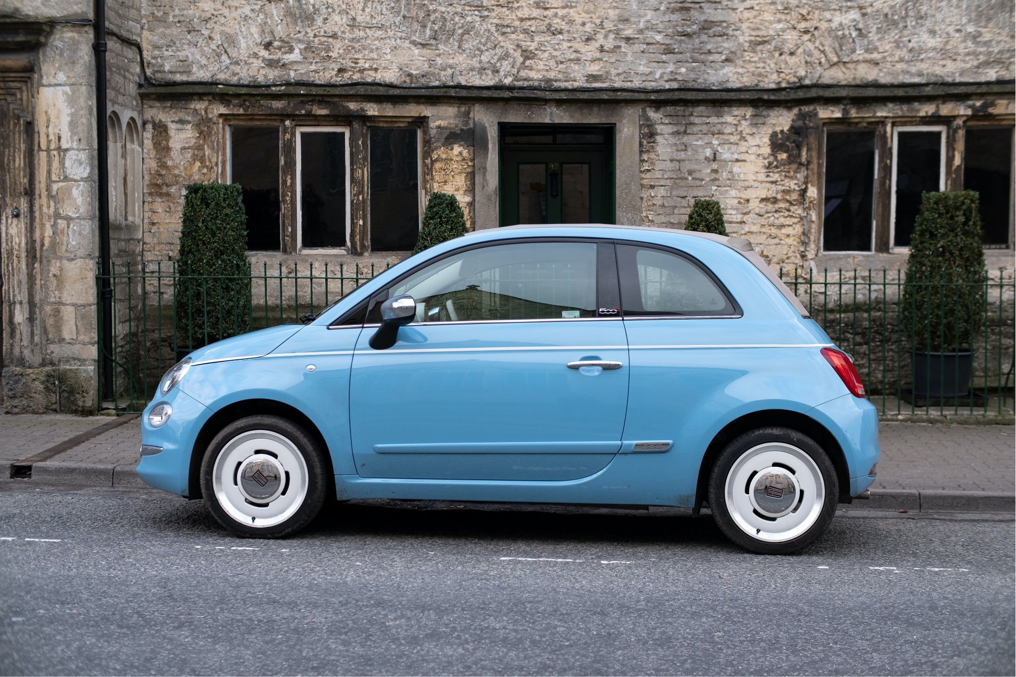 A small blue car parked in front of a traditional English country cottage.